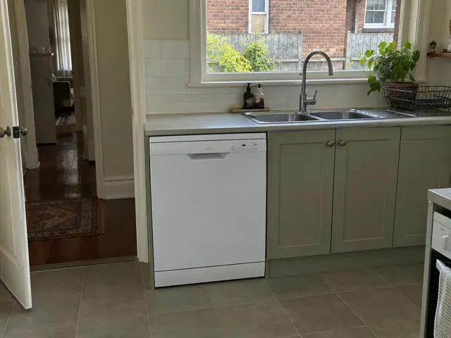 Kitchen sink area with a built-in dishwasher under a benchtop beside a window in a tiled home interior in Wickham