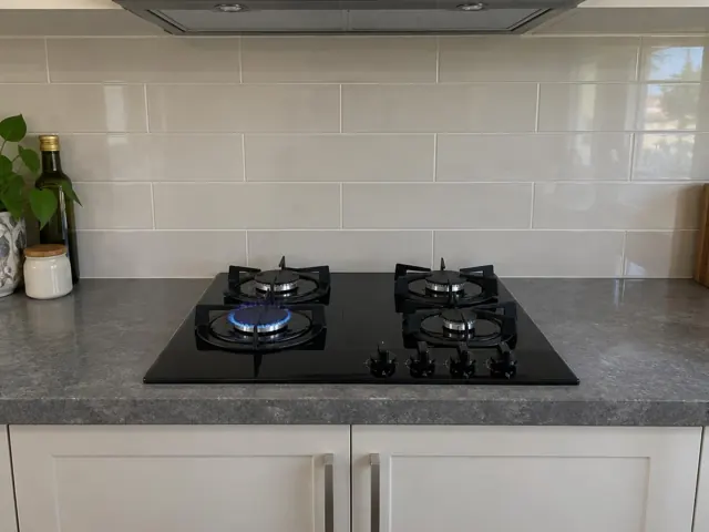 Black gas cooktop set into a grey benchtop with white tiled splashback in a modern kitchen in Hamilton